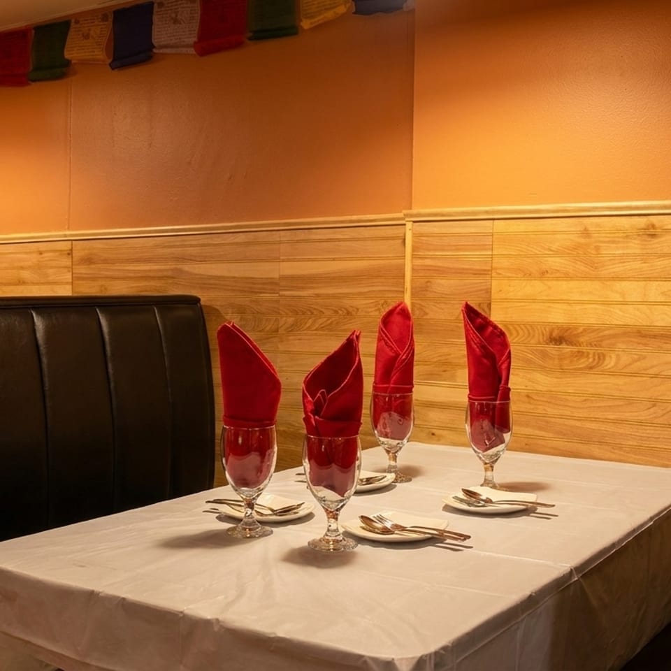 Restaurant booth with a set table, red napkins in glasses, and prayer flags overhead.