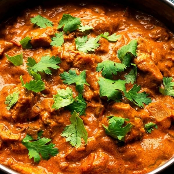 Close-up of a metal bowl filled with vibrant orange chicken curry, garnished with fresh green cilantro.