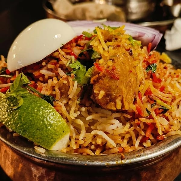 Chicken biryani in a copper pot, garnished with a hard-boiled egg, lime, and red onion.