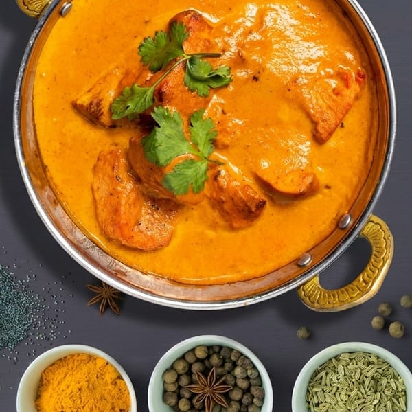 Overhead view of chicken tikka masala in a copper pot, surrounded by spices.